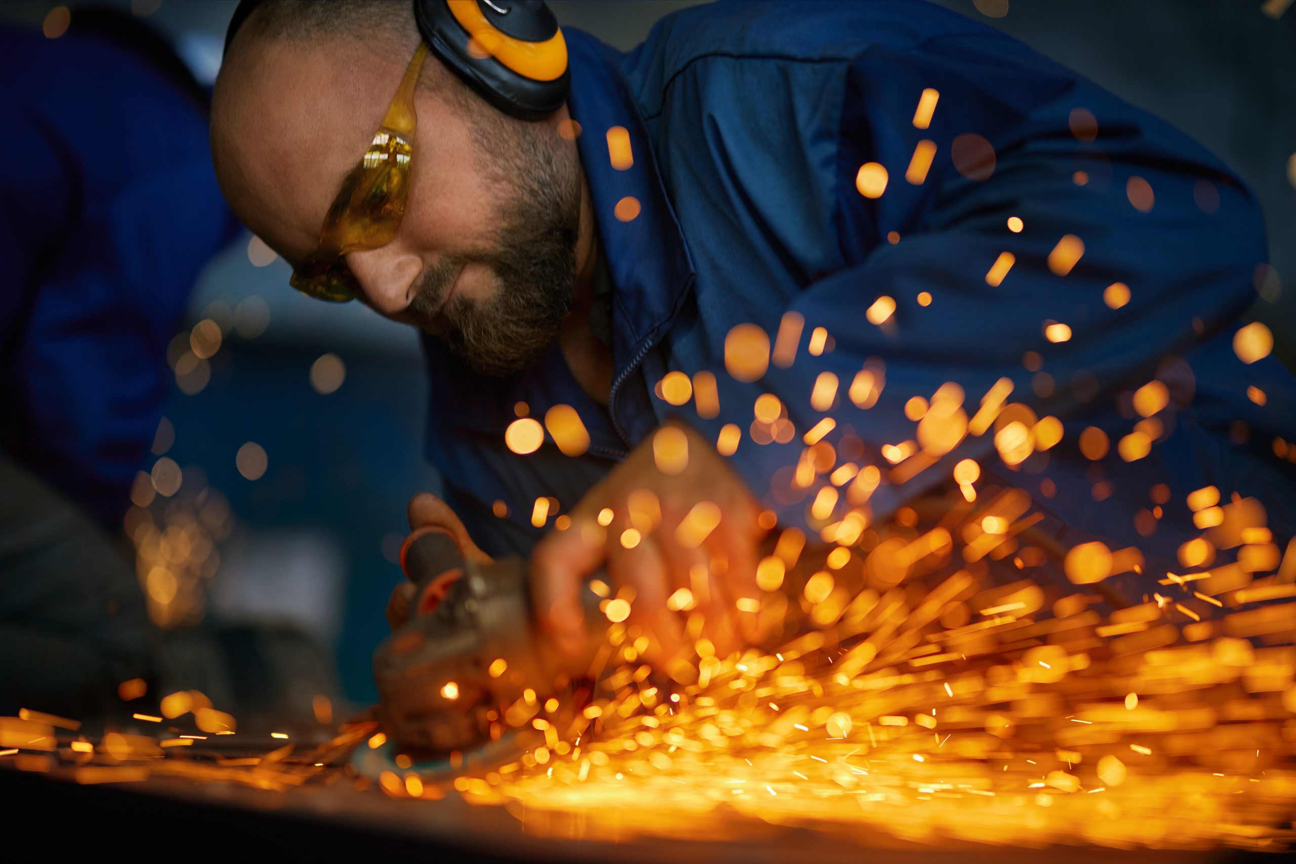 Close up of worker with headphone in dark blue uniform doing gate by electric steel cutter machine for welding special metal. Concept of process produce modern fence in garage.